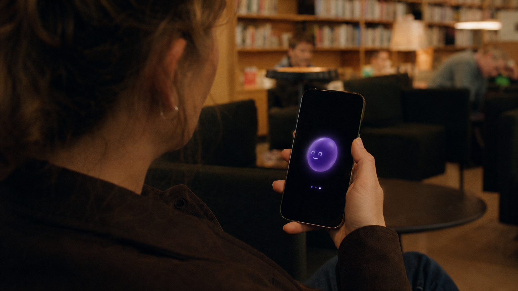 En person står med telefonen i hånden i et bibliotek og venter, mens OPPA lyser på skærmen.